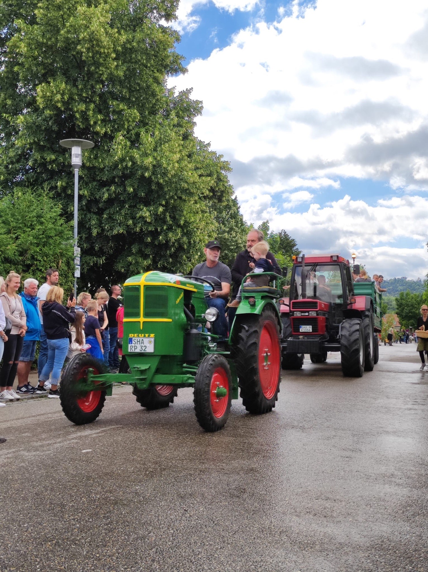 Grüner Deutz-Oldtimer und roter Traktor fahren an Zuschauern am Straßenrand vorbei