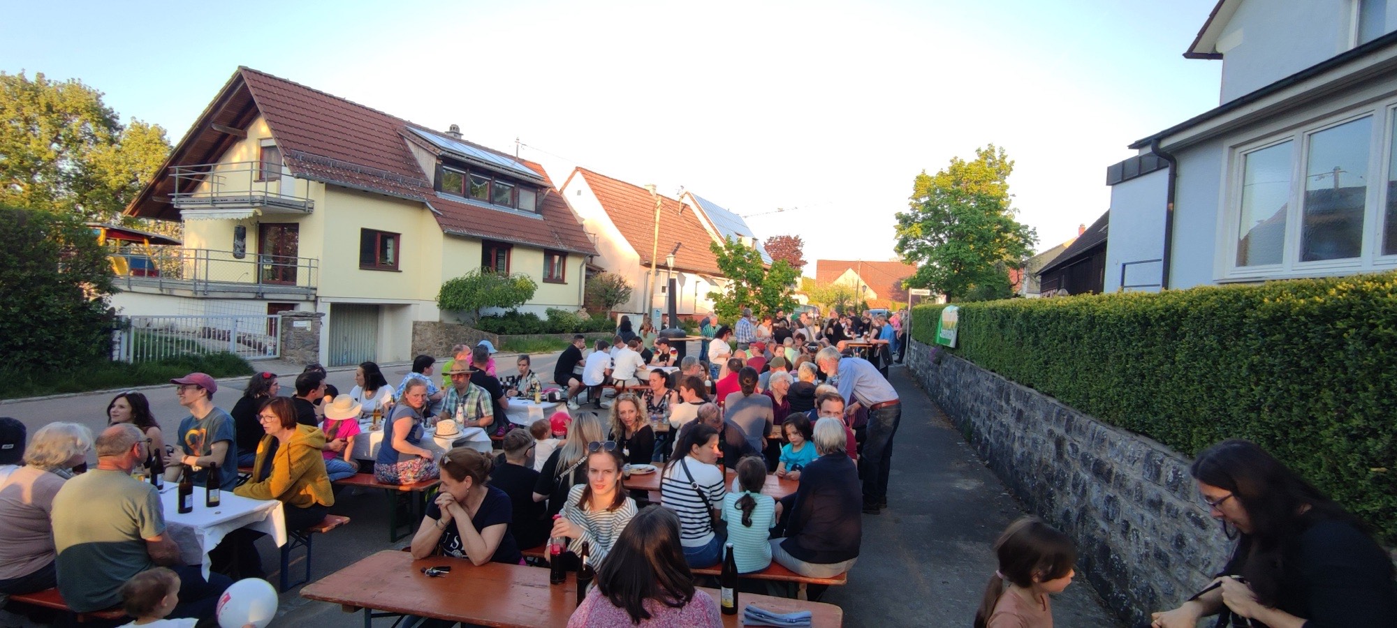 Voll besetzte Biertische auf der Dorfstraße in der Abendsonne